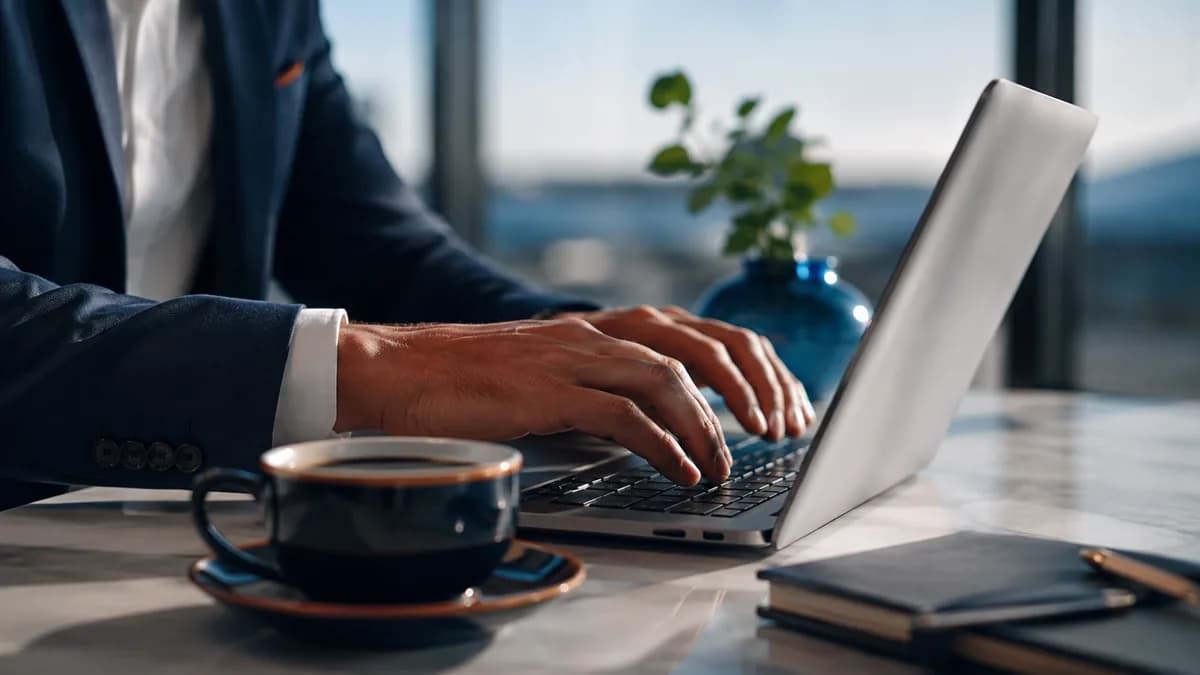 Mains sur un clavier d'ordinateur avec une tasse de café, illustrant la rédaction d'un modèle d'email de remboursement